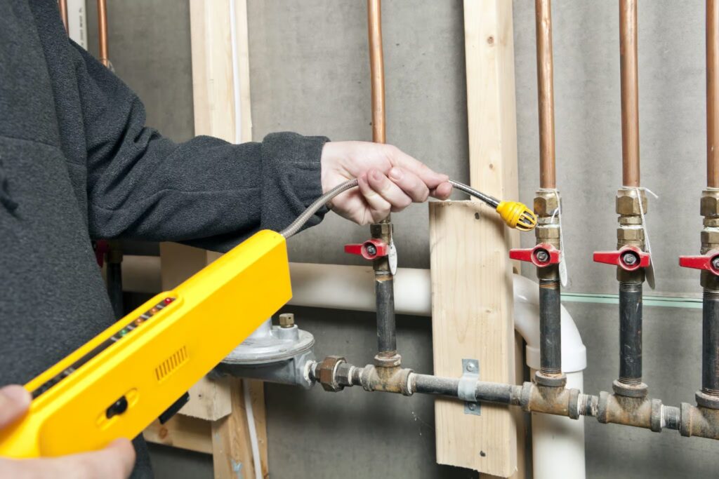Technician using gas leak detection equipment on plumbing system with copper pipes and valves.